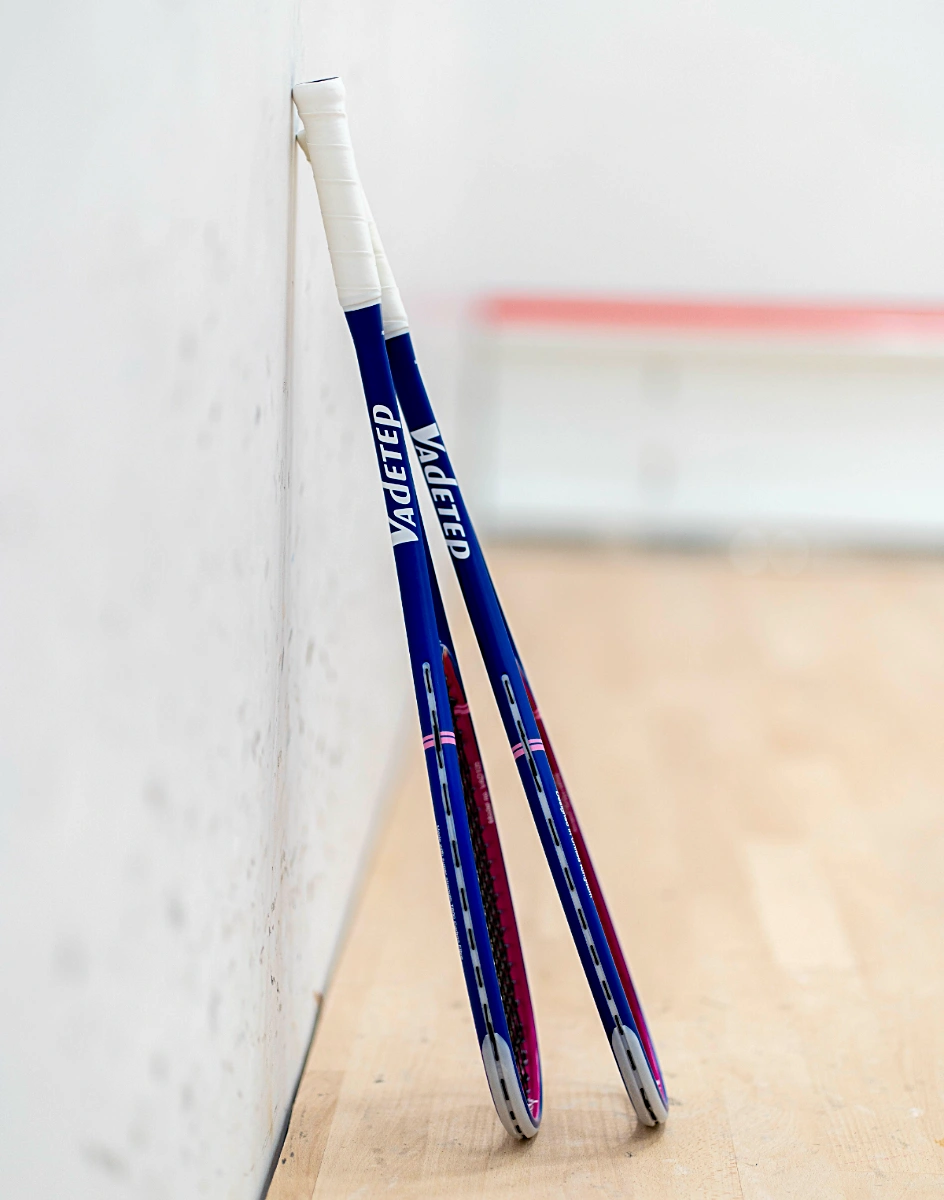 Two Vadetep 105 squash rackets leaning against squash court wall